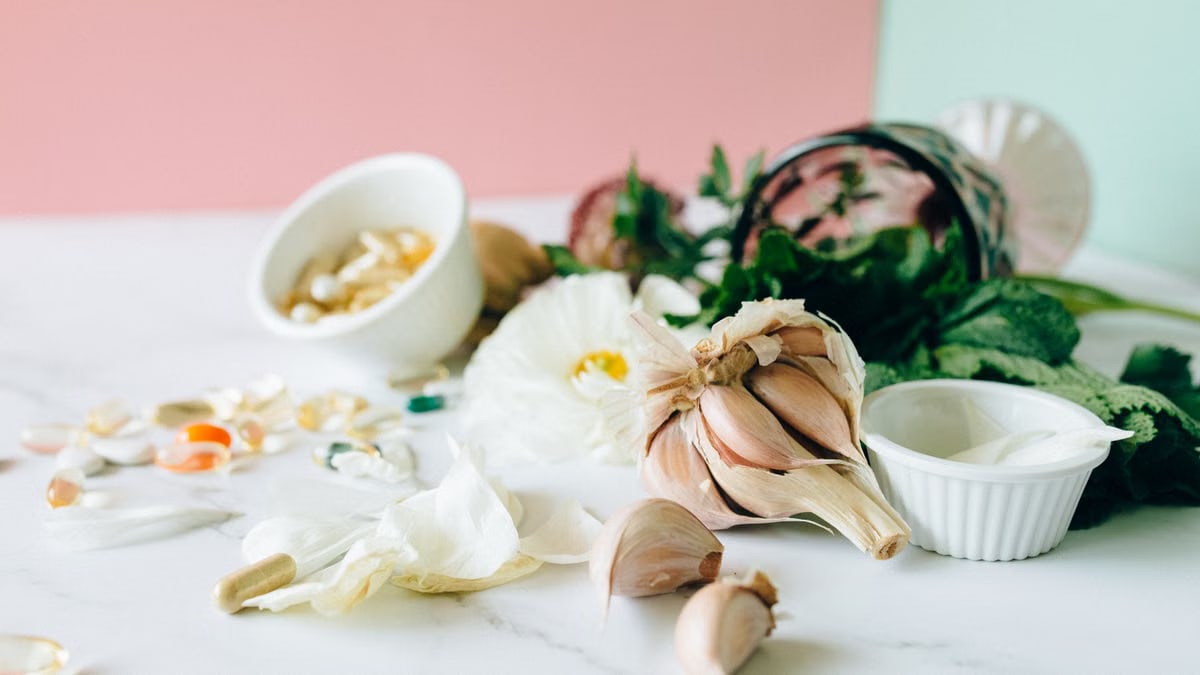 Flat lay of garlic, supplements, and herbs showcasing natural remedies on a marble surface.